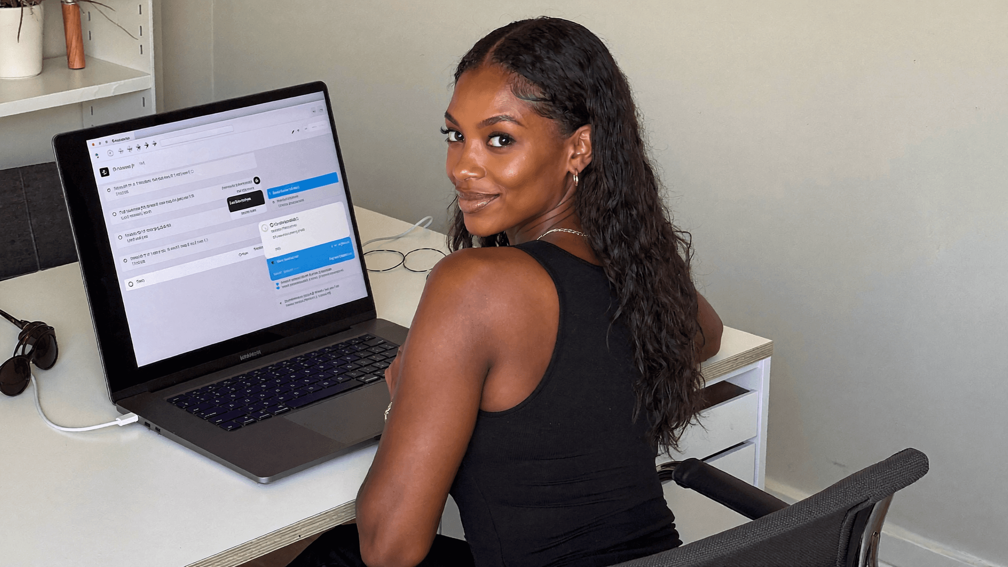 a young woman sat a desk, looks back over her should smiling in a confident and accomplished manner.