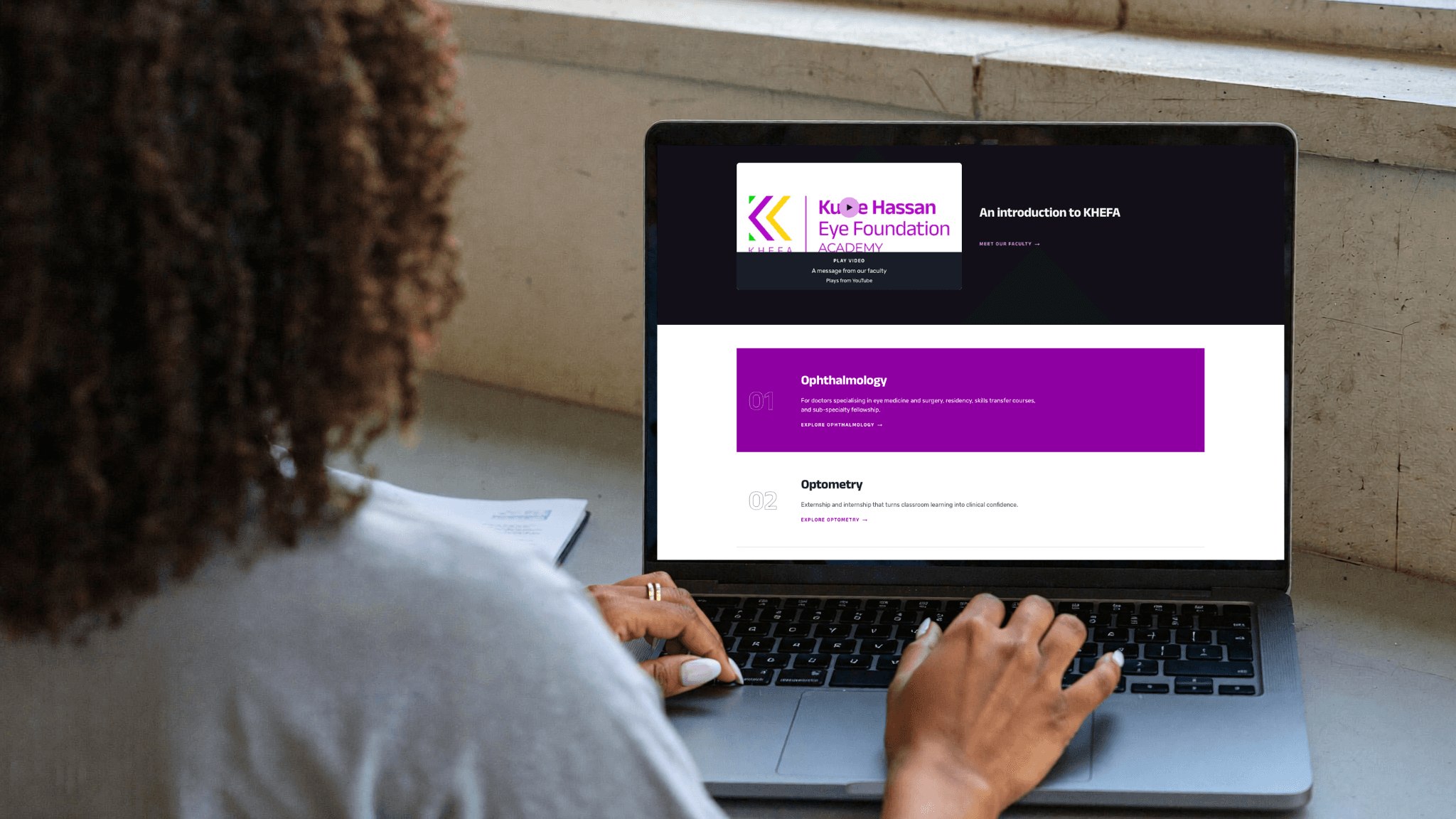 A black woman with curly hair is viewing a laptop screen with the KHEFA Course Catalog on screen 